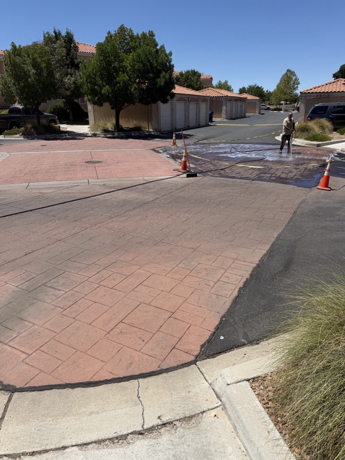 Pressure washing a stamped concrete driveway, half cleaned showing the dramatic before and after contrast